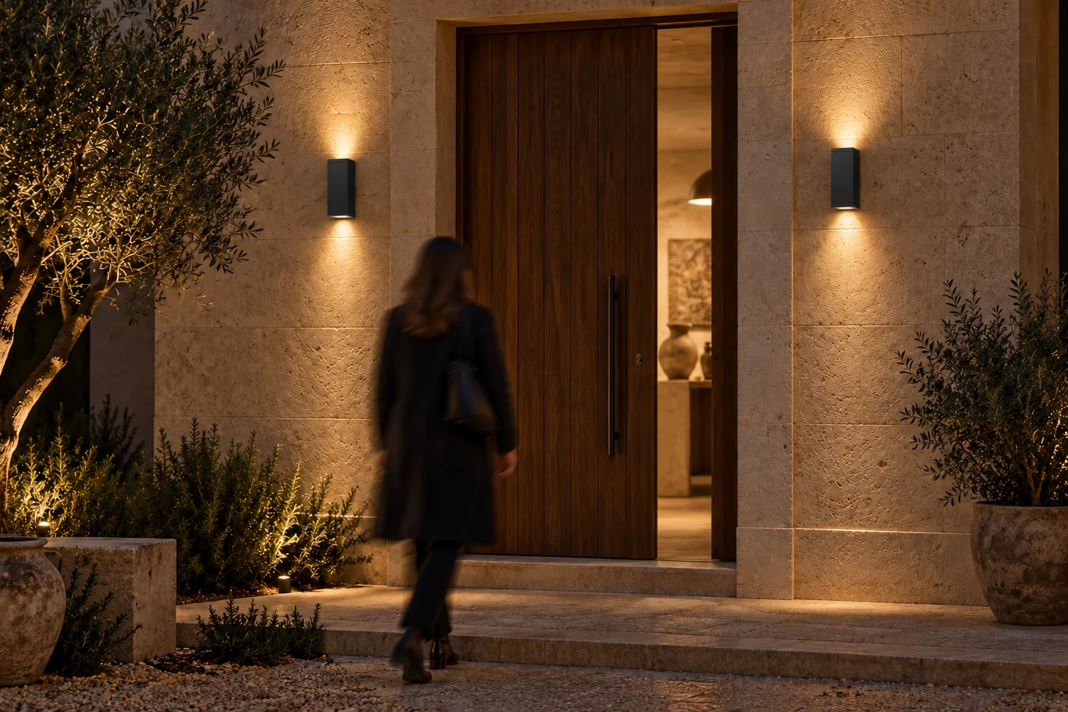 Idea notturna di ingresso d’atelier con due applique WALL AB MEDIUM nere a doppia emissione ai lati della porta e una persona in movimento