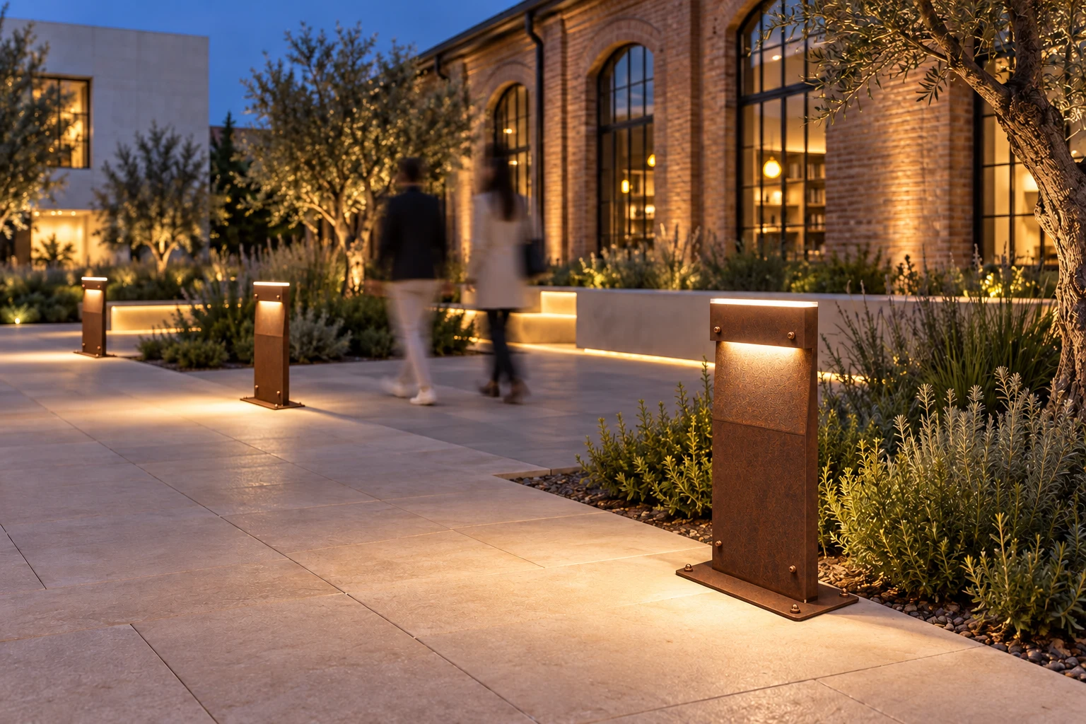 Idea notturna di piazza con bollard DOLMEN base in proposta di finitura corten e dettagli color rame, persone sfocate