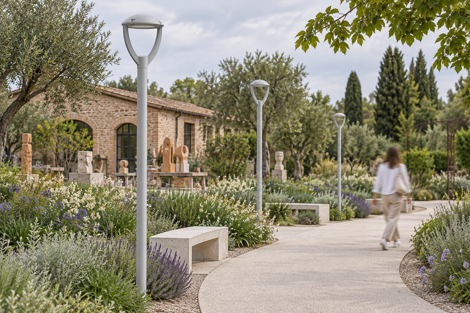 NEWTON Small Top Pole spento in un giardino d’arte, con calotta grigio chiaro e due bracci curvi aperti riferiti alla fotografia originale Small TP. La scena non attesta taglia né misure: revisione e dimensioni vanno verificate con l’ufficio tecnico; altezza e supporti del palo sono illustrativi.